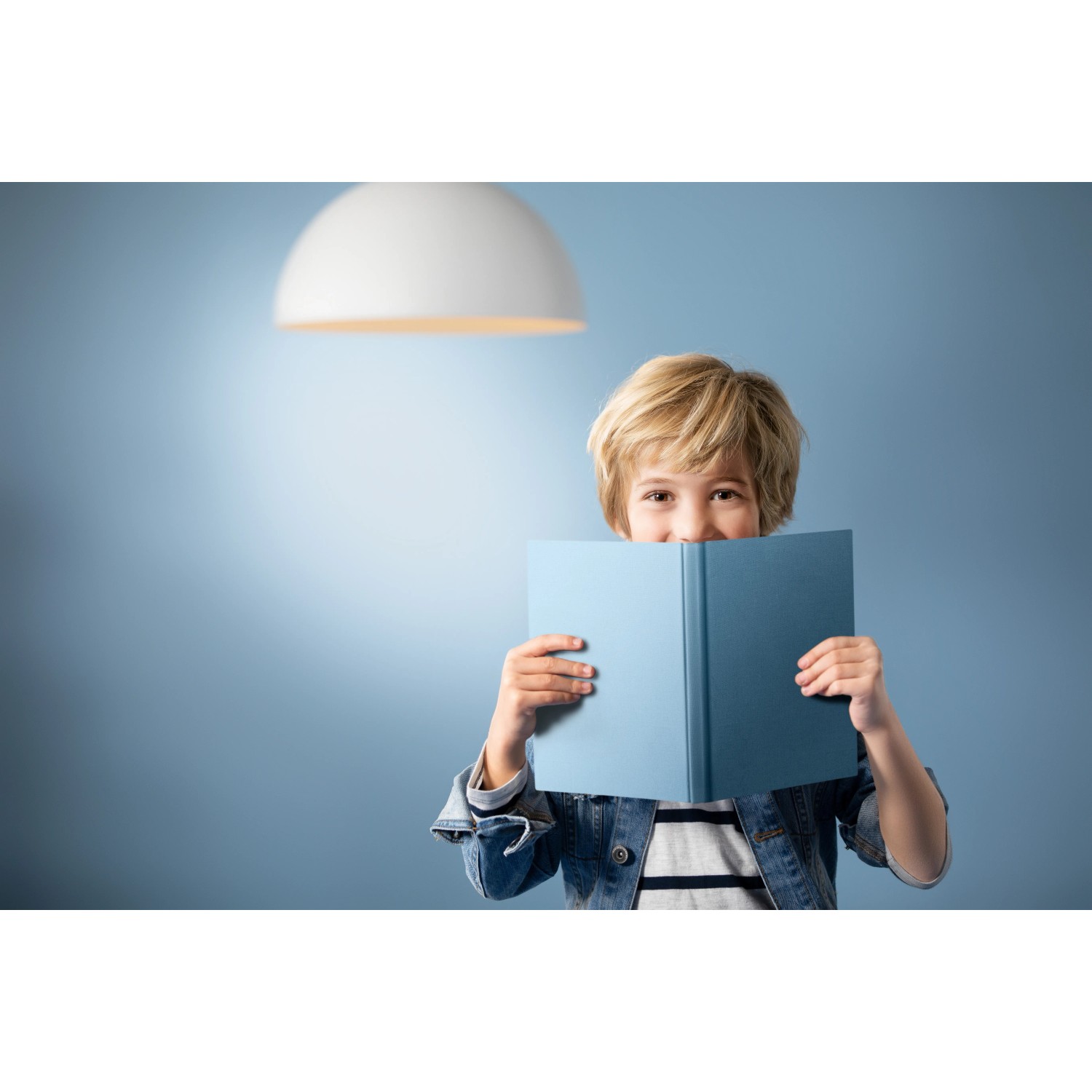 Philips LED E14 Tropfenlampe, 6,5W, unter einer weißen Hängelampe liest ein Kind ein blaues Buch.