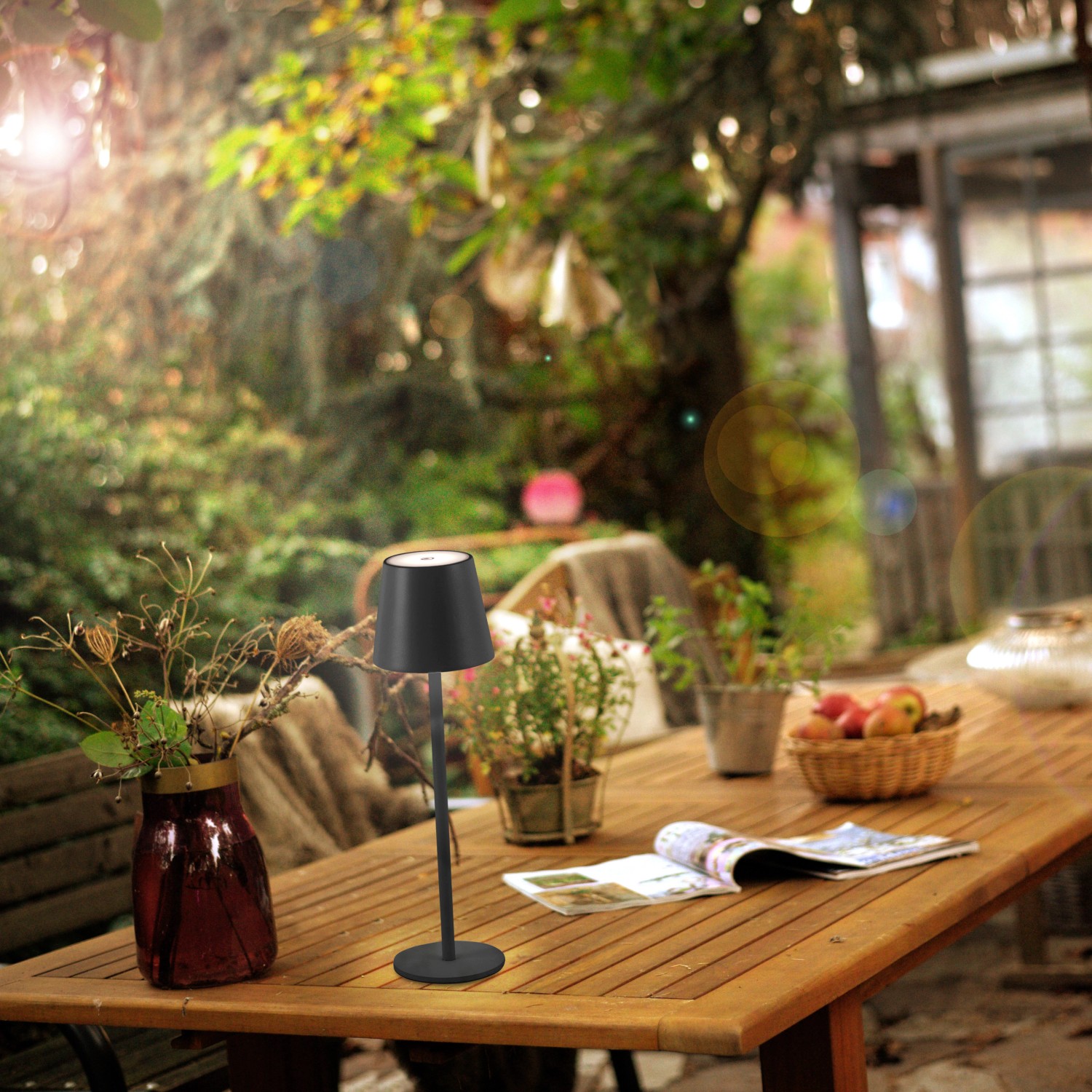 Schwarze LED-Akku-Tischleuchte Euria von Just Light auf einem Gartentisch.