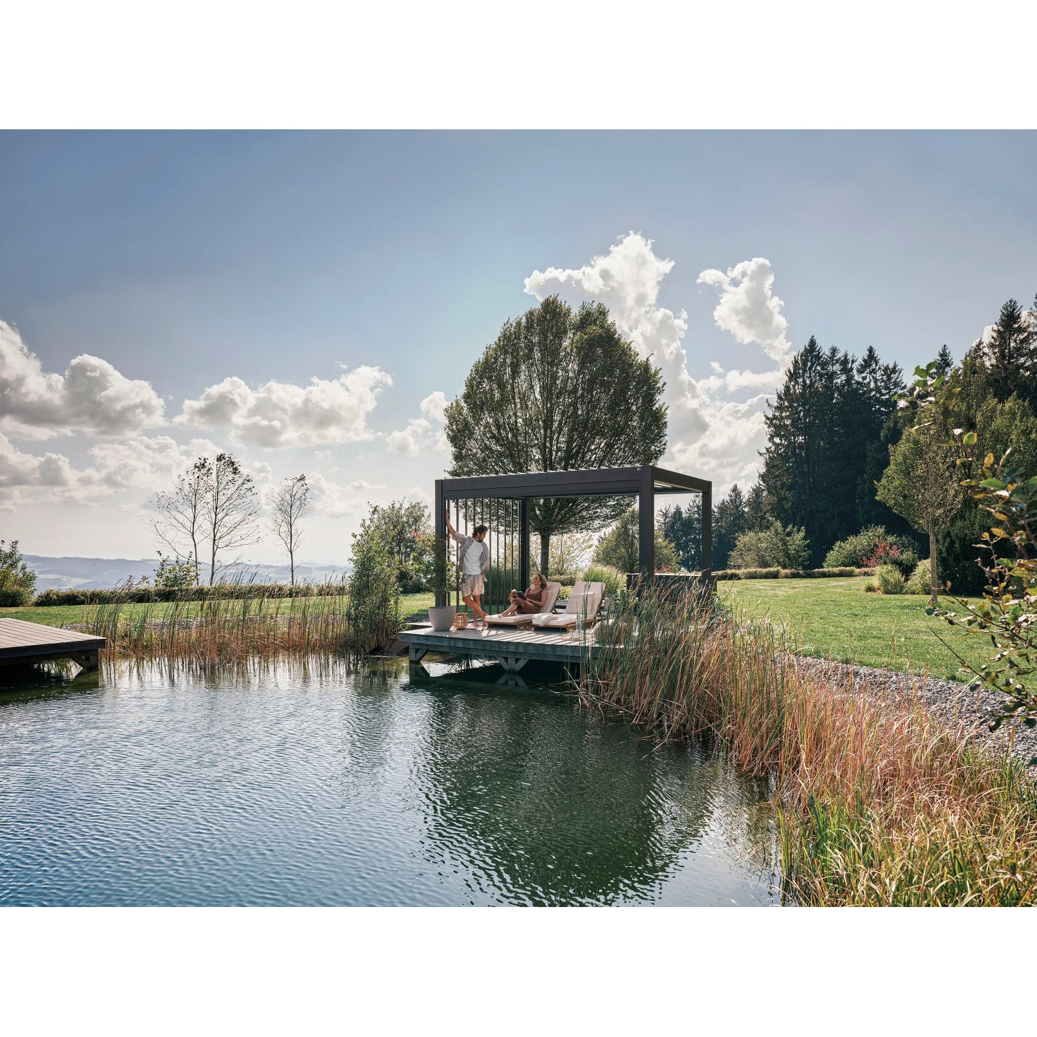 Biohort Pergola in Dunkelgrau/Silber-Metallic am See, Paar entspannt auf Liegen.