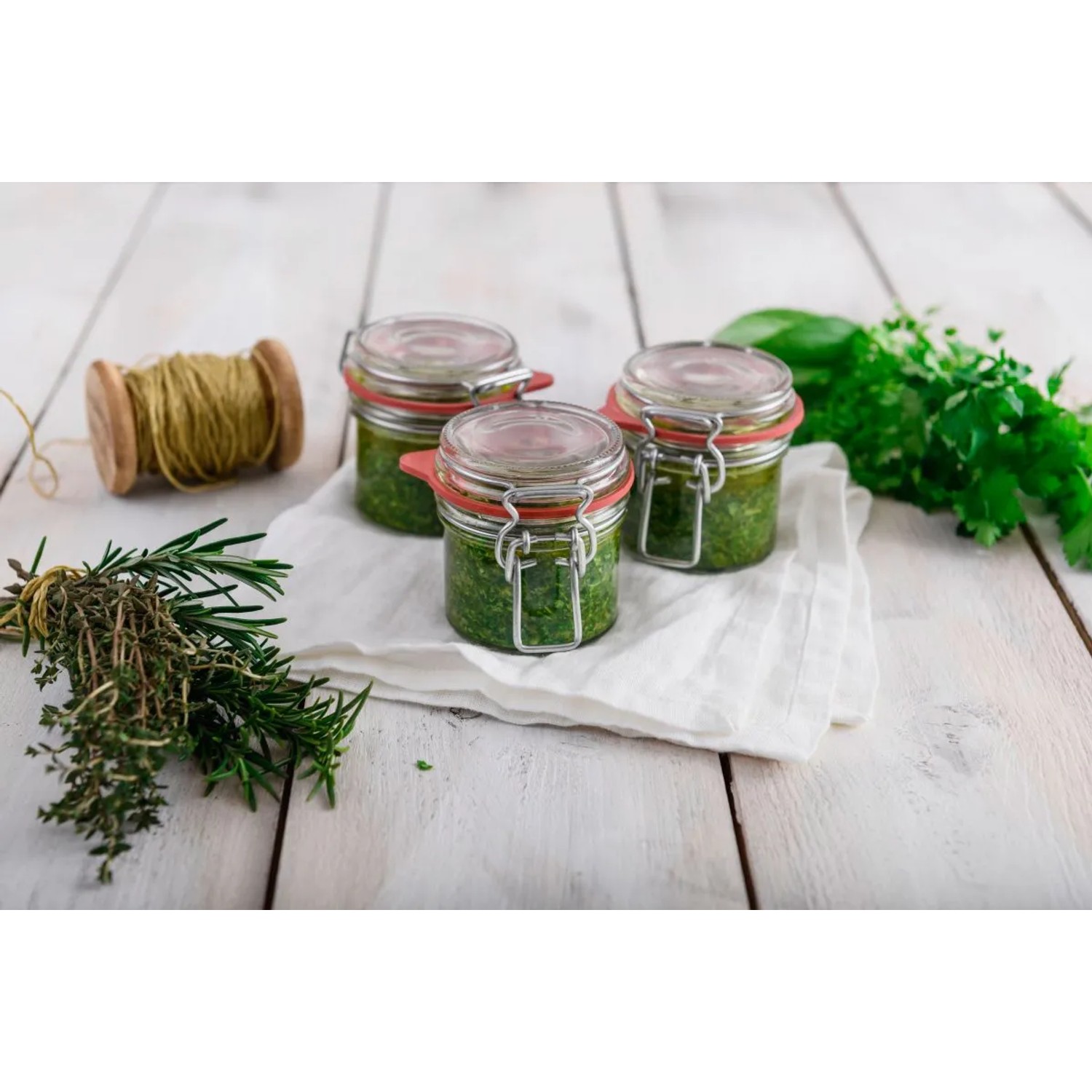 Drei Dr. Oetker Bügelverschlussgläser (135ml) mit Pesto auf weißem Tuch. Küchenhelfer zum Einkochen.