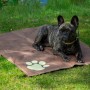 Braune Kühlmatte für Hunde (99,5x70cm) mit Pfotenmuster. Hund liegt entspannt auf der Matte im Garten.