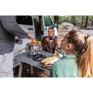 Petromax Atago Gasgrill beim Camping: Kompakter Edelstahl-Grill mit Grillgut und Personen.
