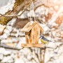 Geflammtes Vogelfuttersilo Cottage aus Holz mit Blaumeise im Winter.