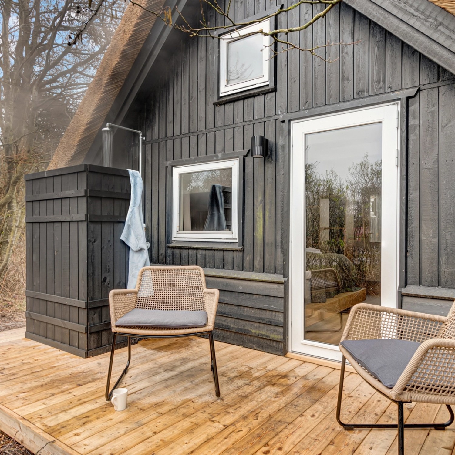 Schwarzer Sichtschutzzaun Rustik aus Nadelholz vor einem Haus mit Reetdach und Gartenmöbeln.