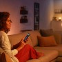 Frau steuert Philips Hue LED Filament Lampe E27 mit dem Smartphone im Wohnzimmer.