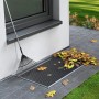 tesa® Insect Stop Lichtschachtabdeckung aus Edelstahl mit Laub und Rechen vor Kellerfenster.