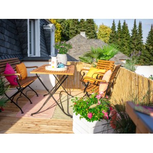 Balkon mit Schilfrohrmatte als Sichtschutz, Gartenmöbeln und Pflanzen.