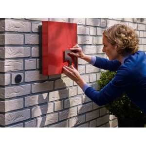 Frau befestigt Hausnummer mit Tesa Montageband auf Mauerwerk.