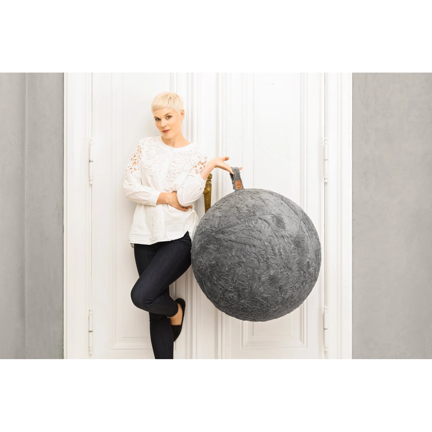 Sitting Ball Hocker Fluffy, mittelgrau, 150 l, mit Tragegriff und Frau an einer Tür lehnend.