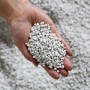 Nahaufnahme: Hand hält graues Stein- und Recycling-Kunststoff-Granulat für Ecopots Pflanztöpfe.