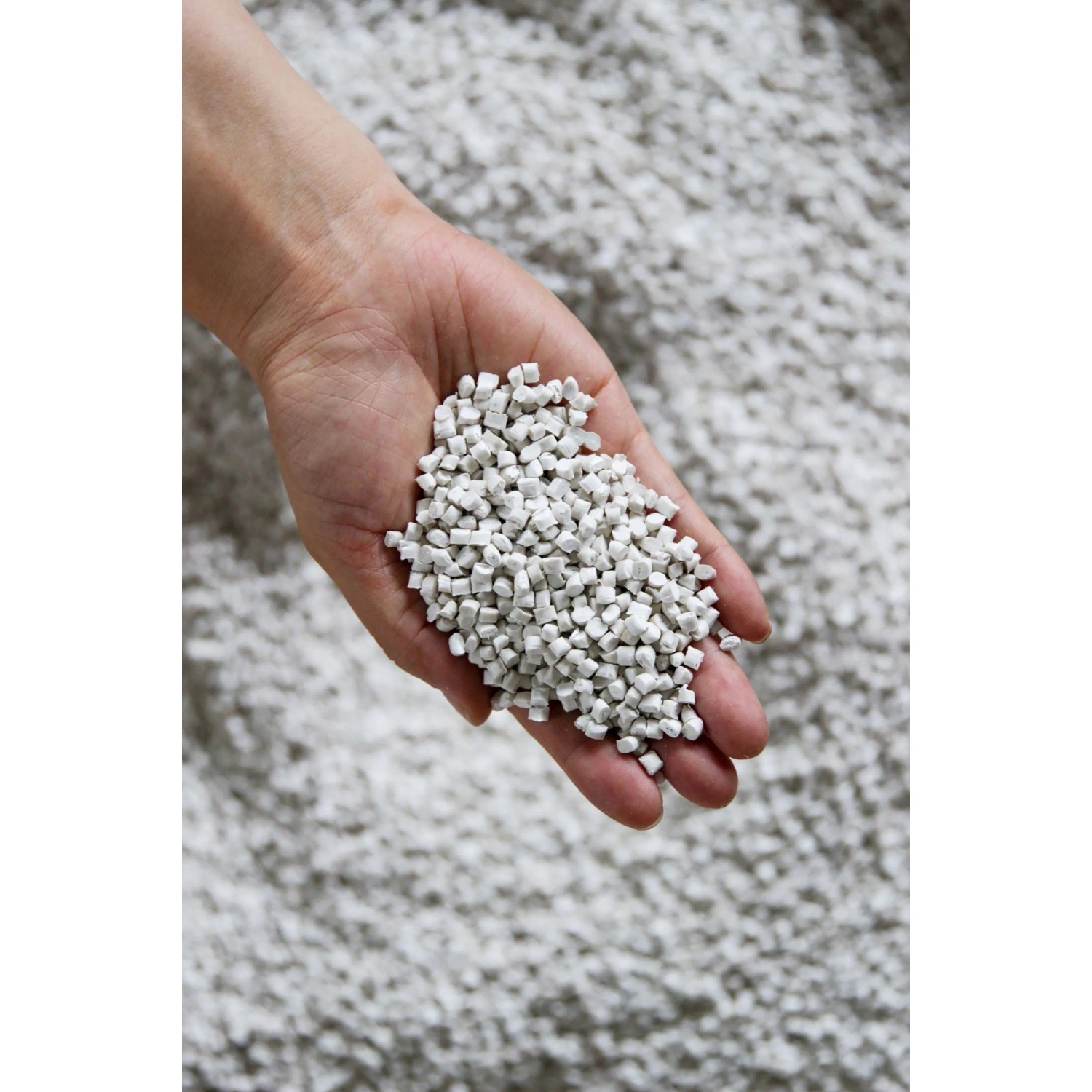 Nahaufnahme: Hand hält graues Stein- und Recycling-Kunststoff-Granulat für Ecopots Pflanztöpfe.