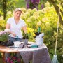 Frau beim Umtopfen von Blumen auf einem Tisch mit LUX Abdeckvlies als Unterlage.