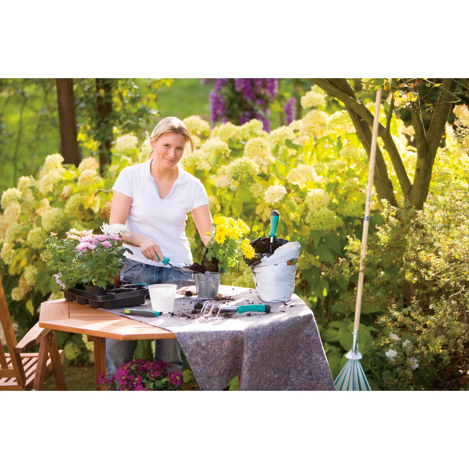 Frau beim Umtopfen von Blumen auf einem Tisch mit LUX Abdeckvlies als Unterlage.