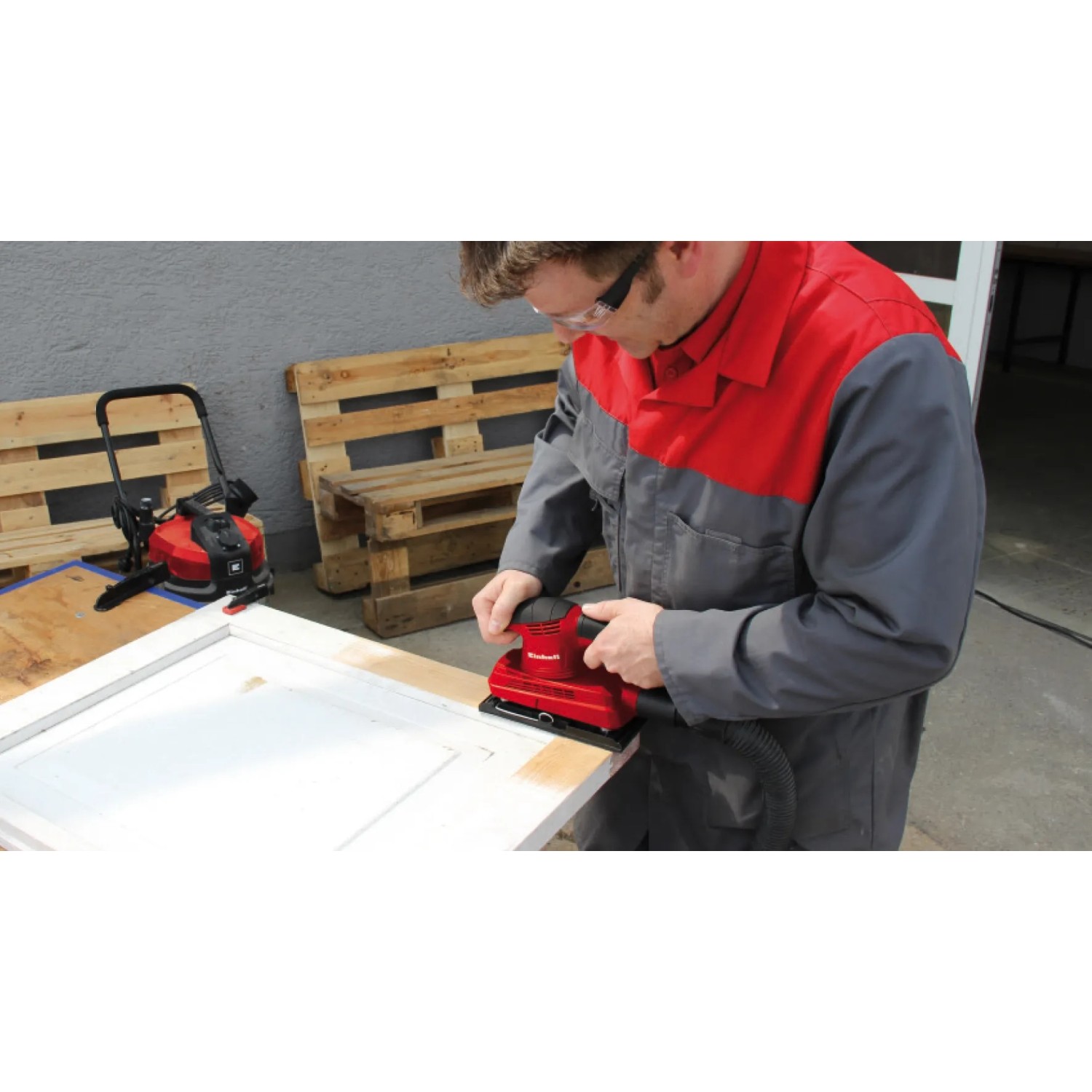 Einhell TC-OS 1520 Schwingschleifer in Nutzung auf einer Tür, rote Schleifmaschine mit Staubabsaugung.