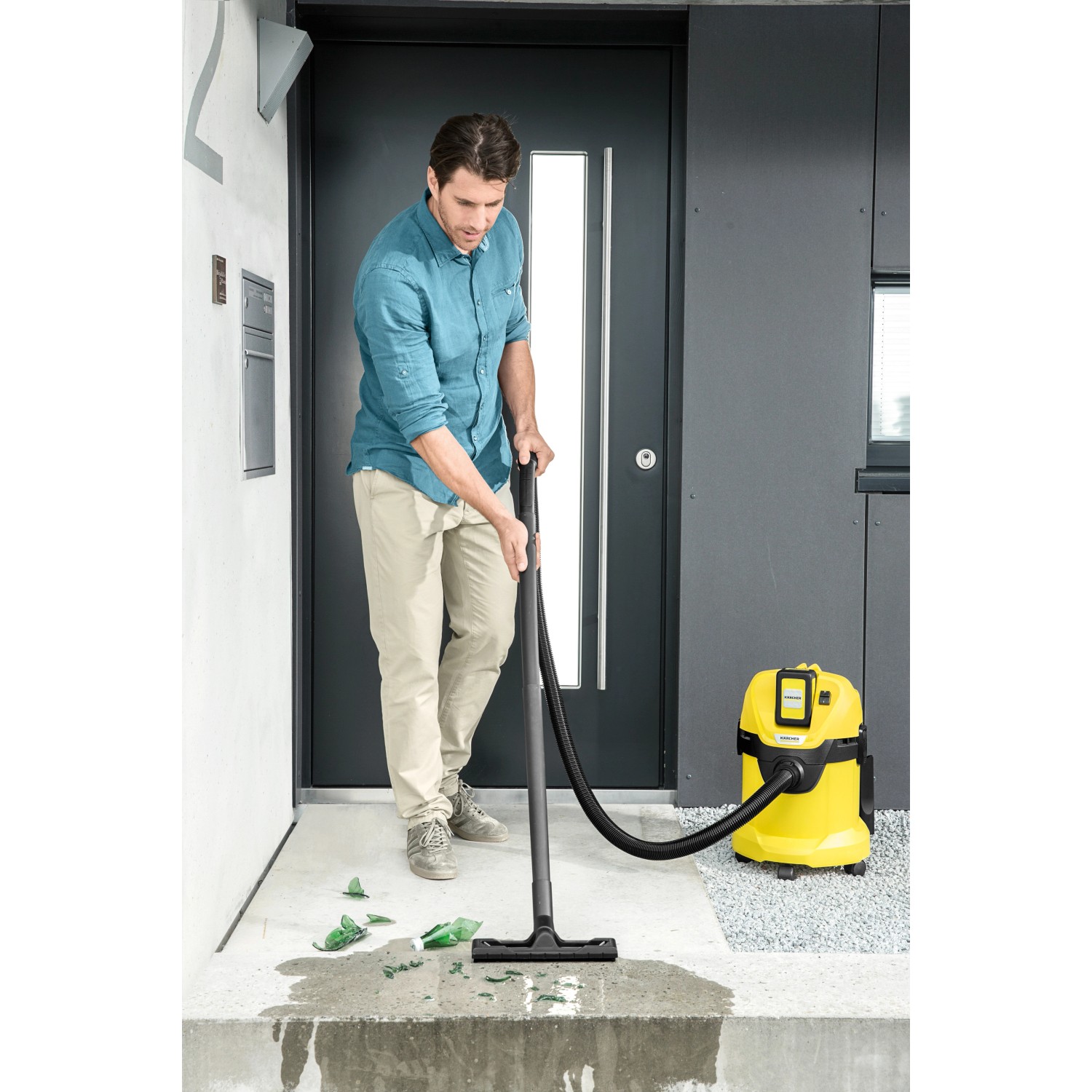 Mann saugt mit Kärcher Akku-Mehrzwecksauger WD 3 Battery Glasscherben und Wasser vor einer Haustür.