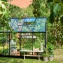 Schwarzes Halls Gewächshaus Qube 68 (5 m²) im Garten mit Pflanzen und Gartentisch.