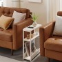 Schmaler, grauer Songmics Nachttisch mit Ladefunktion neben braunem Sofa.