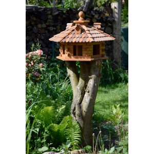 Rustikales XXL-Vogelfutterhaus im Blockhaus-Stil mit Holzschindeldach auf Baumstumpf im Garten.