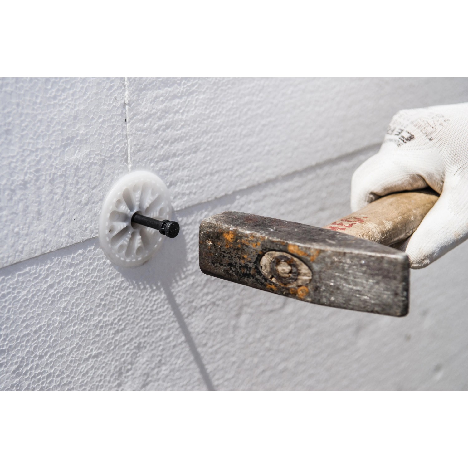 Einbau eines Thermomaster D-Plus Dämmstoffdübel mit Hammer in eine weiße Dämmplatte.