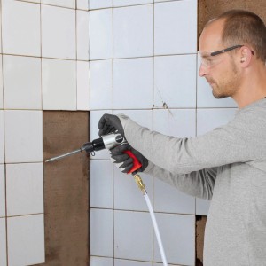 Mann mit Drucklufthammer beim Fliesenschlagen. Kompressor Zubehör für Abbauarbeiten.