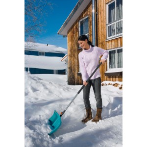 Frau benutzt Gardena combisystem Alustiel 130 cm mit Schneeschaufel zum Schneeräumen vor einem Haus.