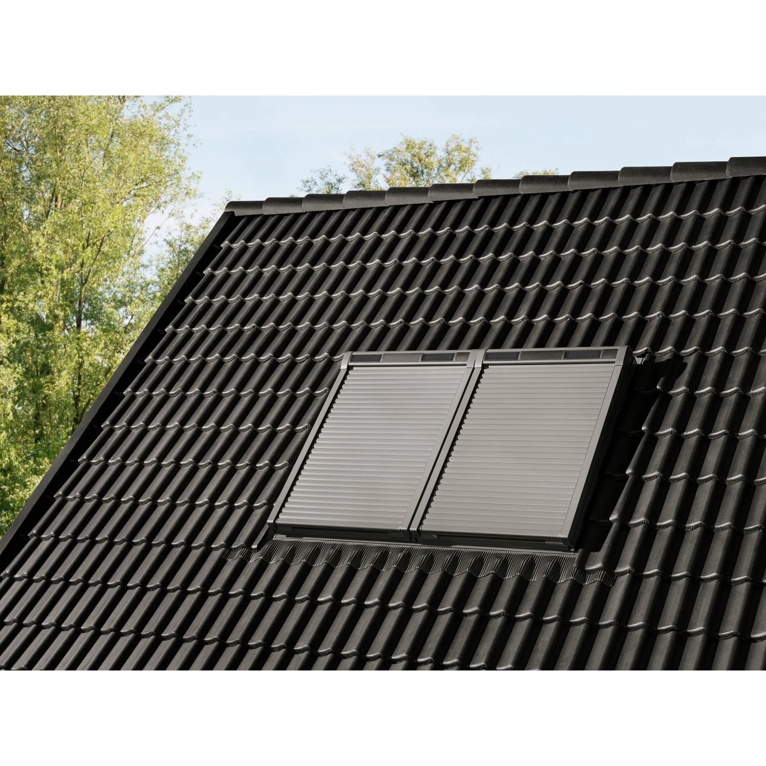 Alufarbener Rolladen Solarantrieb Modular CK02 auf einem Dachfenster montiert.
