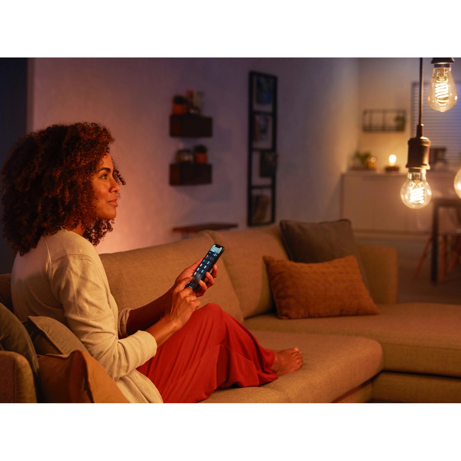 Frau steuert Philips Hue Filament Lampe E27 mit dem Smartphone im Wohnzimmer.