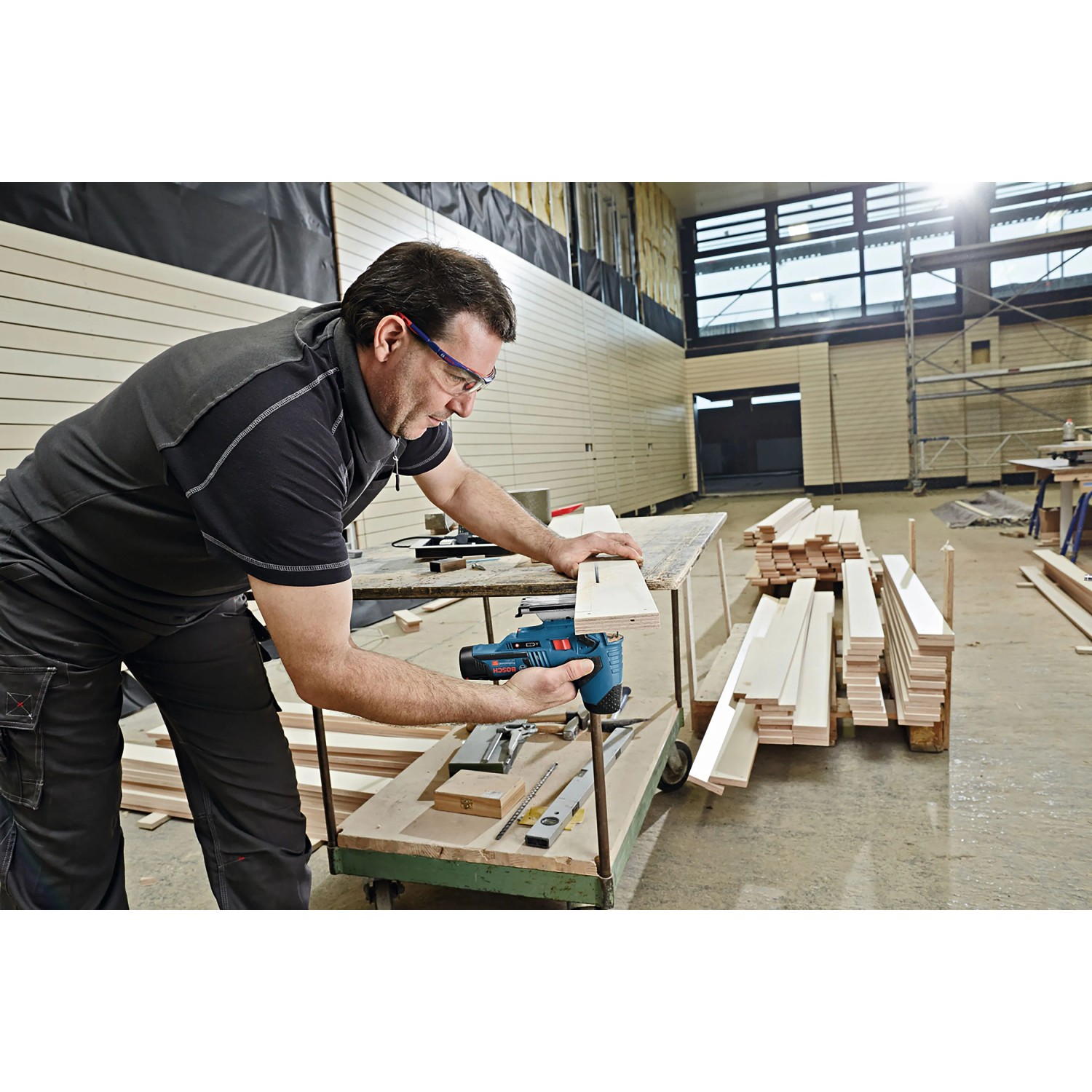 Mann sägt Holz mit Bosch Professional Akku-Stichsäge GST 12 V-70 in Werkstatt. Präzise Schnitte für Holzbearbeitung.
