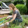 Frau nutzt Gardena Combisystem Drahthandfeger zur Beetpflege im Garten.