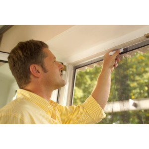 Mann befestigt weißes Tesa Fliegengitter mit Klettband an einer Tür.