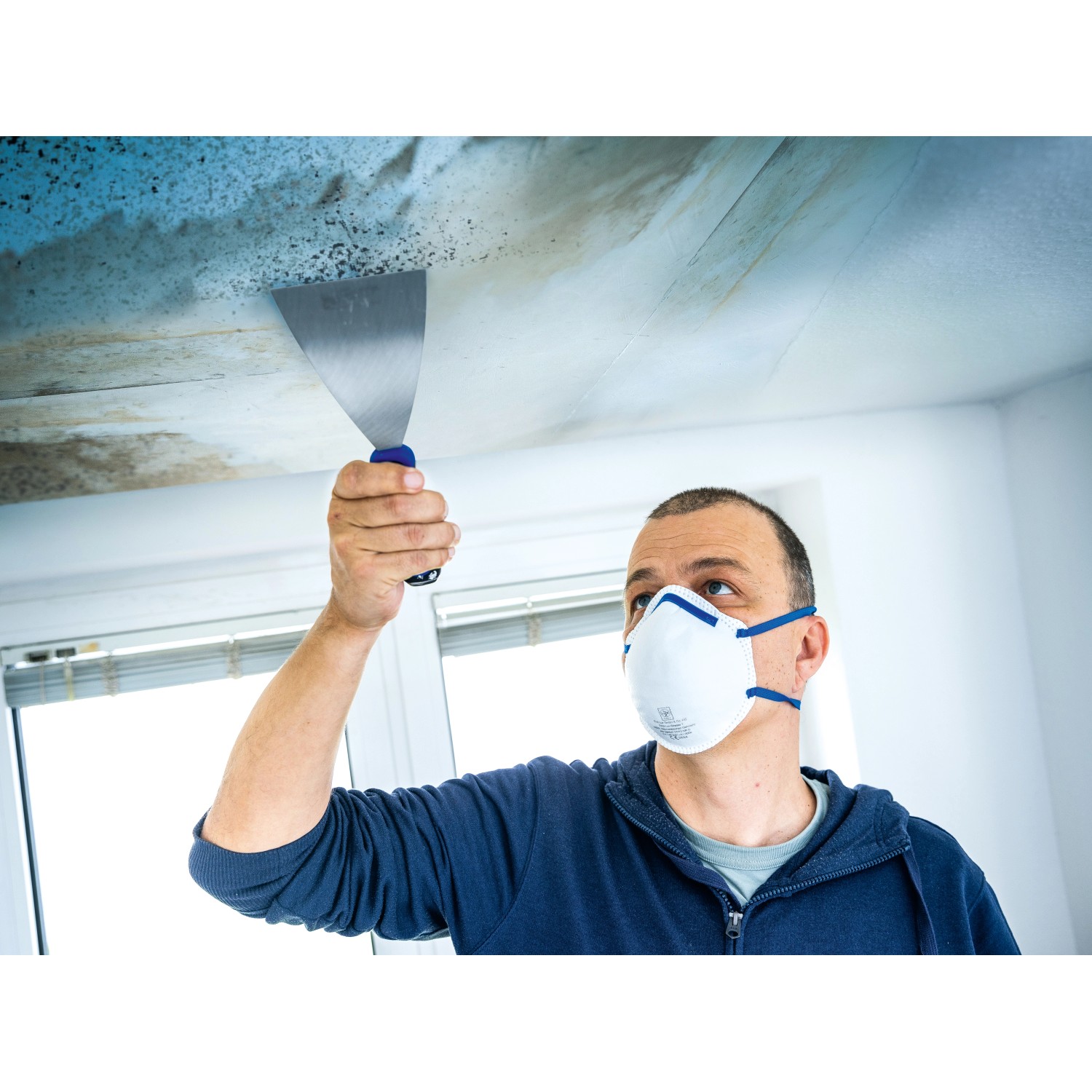 Mann mit LUX Feinstaubmaske FFP2 beim Entfernen von Schimmel an der Decke.
