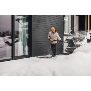 Mann räumt mit Fiskars Schneeräumer Solid Schnee vor Haus. Schneeschieber mit D-Griff.
