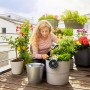 Frau installiert Gardena Solar-Bewässerung Aqua Bloom Set auf Balkon mit Pflanzen.