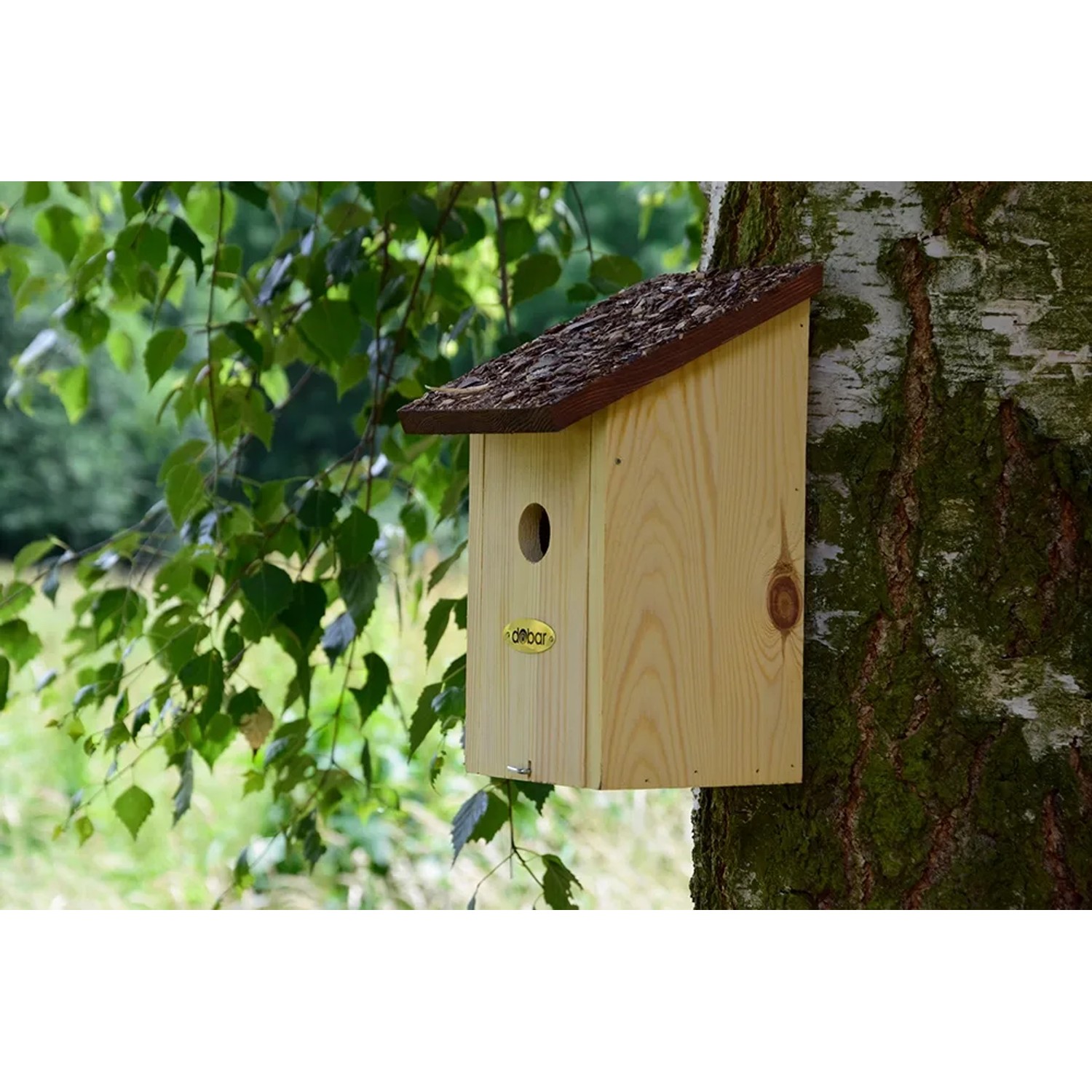Nistkasten aus Kiefernholz mit Rindendach am Baum befestigt.