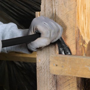 Hand mit Handschuh nutzt schwarzes Brecheisen, um Holzbretter zu hebeln. Vielseitiges Werkzeug für Abbrucharbeiten.