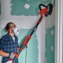Mann schleift Wand mit Einhell Trockenbauschleifer und Schleifgitter-Set, Ø 225 mm.