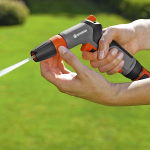Gardena Gartenspritze Classic in Aktion: Graue Spritze mit orangenen Akzenten wird von Hand bedient, Wasserstrahl sichtbar.