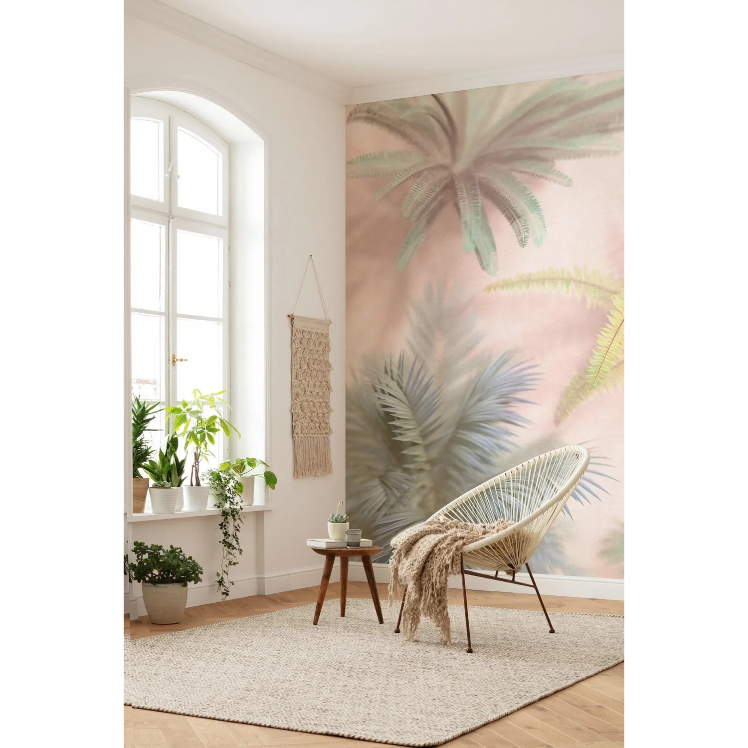 Wohnraum mit Komar Vliestapete Vague Botany in Pastellrosa mit Palmenmotiv.