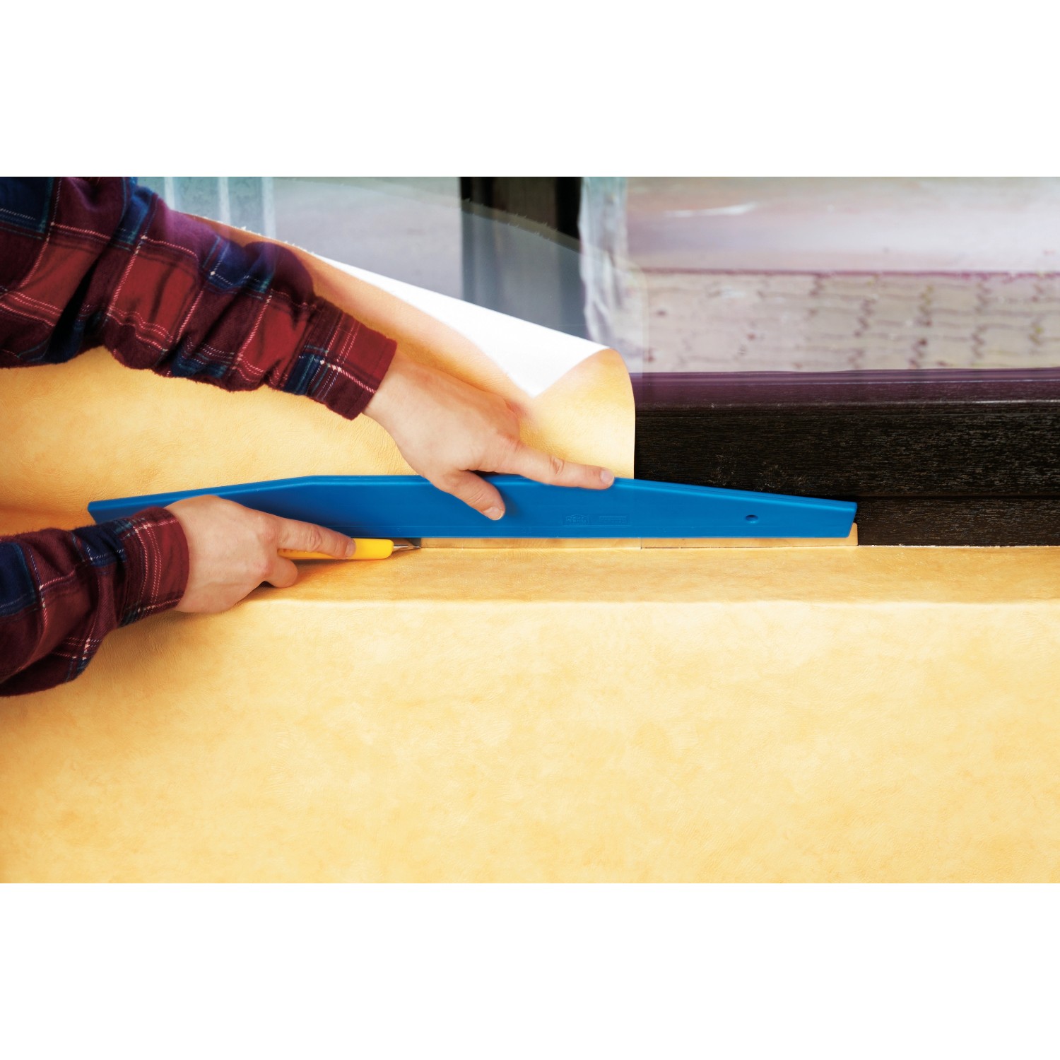 LUX Beschneidelineal 60 cm im Einsatz: Tapete zuschneiden mit Cuttermesser. Tapezierwerkzeug mit blauem Griff.