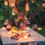 Gartenparty-Szene mit weiß lackiertem Tisch, Wein, Käse und Kerzen im Garten.