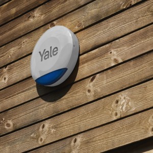 Yale Außensirene, kabellos, grau, montiert auf Holzwand. Smart Alarm System für den Außenbereich.