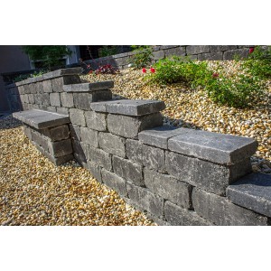 Anthrazitfarbene Antik-Mauer aus gerumpelten Mauersteinen als Beeteinfassung und Sitzbank.