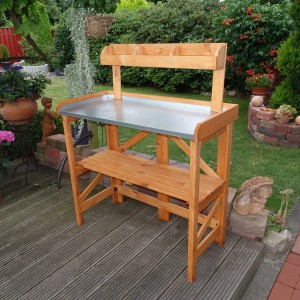 Klappbarer Pflanztisch aus Holz mit verzinkter Arbeitsfläche und Ablage für Gartenzubehör.