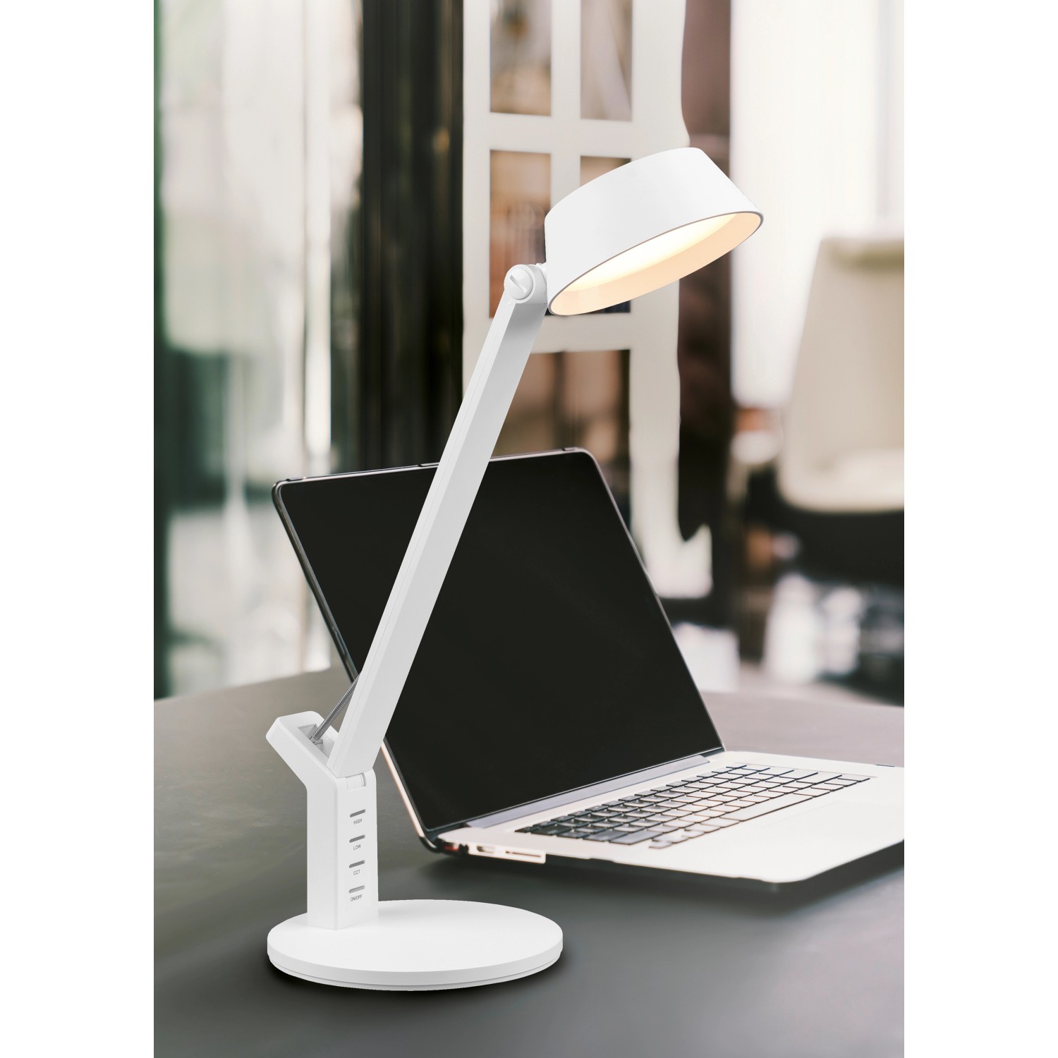 Weiße LED-Tischleuchte Ava von Trio mit USB-Anschluss vor Laptop.