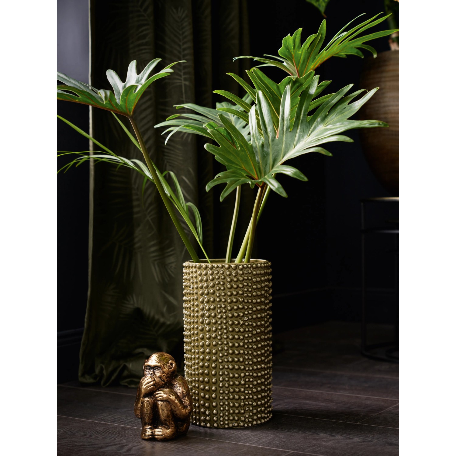 Grüne Vase Dark Wonder (25 cm) mit Noppenstruktur und Zimmerpflanze, neben einer Deko-Affe Figur.