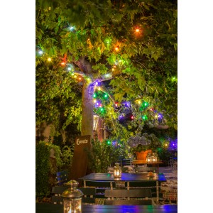 Konstsmide LED Biergartenkette mit bunten Lichtern an einem Baum über einem Tisch im Garten.
