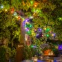 Konstsmide LED Biergartenkette mit bunten Lichtern an einem Baum über einem Tisch im Garten.