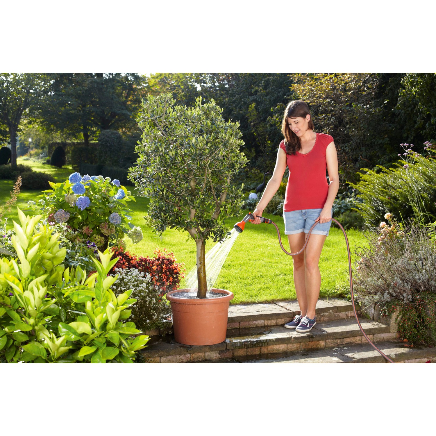 Frau bewässert Baum mit Gardena Classic Multibrause im Garten.