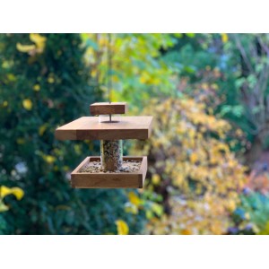 Dobar Vogelfutterhaus aus Eichenholz mit Acrylglas-Silo und Futter vor grünem Hintergrund.