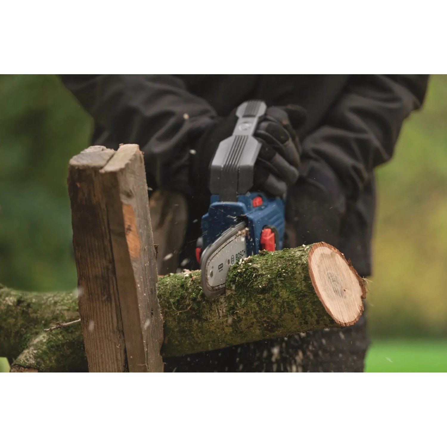 Bosch Akku-Astsäge GKE 18V-15 in Aktion: Bediener sägt Ast mit Akku-Kettensäge im Garten.